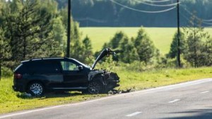 Un VUS noir gravement endommagé à l'avant se trouve sur le bord d'une route rurale en Beauce, entouré d'herbe et d'arbres sous un ciel dégagé. Des débris près du véhicule suggèrent un accident récent, nous rappelant l'importance de l'assurance auto.