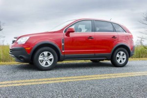 Un VUS rouge, stationné sur une route pavée avec de l'herbe et un ciel nuageux de Beauce en arrière-plan, est vu de côté - une scène idéale pour les amateurs d'assurance automobile.