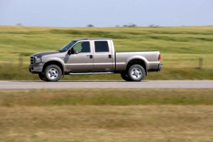 Une camionnette beige roule sur une route rurale de la Beauce, entourée de champs herbeux et d'un ciel clair, une scène paisible où l'on pourrait considérer le coût de l'assurance auto pour de tels déplacements.