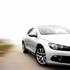 Une élégante voiture de sport argentée est garée sur une route avec un fond blanc, montrant les détails avant et latéraux, y compris les jantes et les phares brillants.