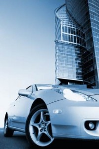 Une voiture de sport argentée est garée devant un bâtiment moderne en verre, photographiée sous un angle bas avec un filtre aux tons bleus froids.