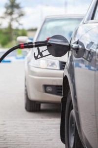 Gros plan d'une voiture en train de faire le plein à une station-service de Sainte-Julie, avec un pistolet à essence inséré dans le réservoir – idéal pour ceux qui envisagent une assurance voiture. Une deuxième voiture est garée en arrière-plan.