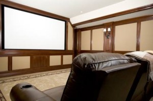 Une salle de cinéma maison avec un grand écran de projection vierge, des sièges inclinables en cuir au premier plan, des boiseries, des murs beiges et un éclairage doux provenant de luminaires muraux : une retraite confortable idéale pour se détendre avec l'assurance habitation pas cher.