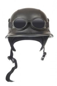 Un casque de moto noir de style vintage avec des lunettes noires attachées et une mentonnière suspendue librement.