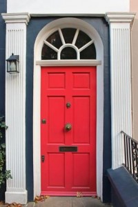Une porte d'entrée rouge vif avec des panneaux décoratifs, un heurtoir en laiton et une fente à lettres, placée dans un cadre blanc avec des colonnes cannelées et une fenêtre en demi-lune au-dessus orne cette maison bleu foncé de Sainte-Julie, parfaite pour vos besoins d'habitation assurés.