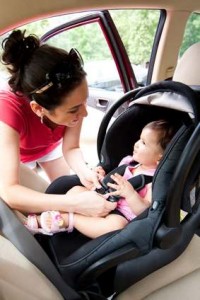 À Sainte-Julie, une femme sourit en installant un bébé dans un siège auto dos à la route. La portière est ouverte et le bébé lève les yeux vers elle. Tous deux semblent heureux et engagés, soulignant l'importance de l'assurance voiture pour les familles.