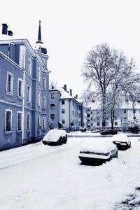 Une rue résidentielle tranquille de Sainte-Rose en hiver, avec des voitures et des bâtiments stationnés sous la neige. Des arbres nus bordent la rue sous un ciel couvert, contribuant à l'atmosphère froide et paisible – un décor idéal pour apprécier Assurance auto.