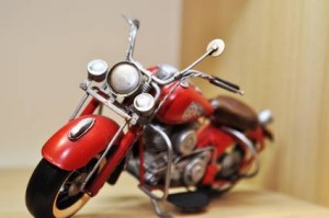Une vue rapprochée d'un modèle de moto rouge vintage exposé à l'intérieur sur une surface en bois clair, mettant en valeur le guidon et les phares détaillés - parfait pour les passionnés à la recherche d'une assurance moto pas cher.