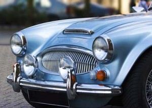 Gros plan de l'avant d'une voiture vintage bleu clair classique, dotée de phares ronds, d'une calandre chromée, de pare-chocs et de phares antibrouillard supplémentaires.