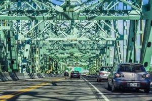 Des voitures circulent sur une route à plusieurs voies sous un pont en treillis d'acier vert à Montréal-Nord, avec des poutres entrecroisées créant un motif géométrique au-dessus de la chaussée - parfait pour ceux qui recherchent une voiture en toute sécurité dans ce quartier animé de la ville.