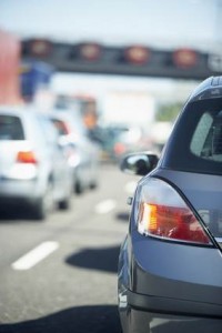 Gros plan sur l'arrière d'une voiture argentée, clignotant droit allumé, dans la circulation sur une route à plusieurs voies ; idéal pour discuter de l'assurance économique ou trouver les meilleures options d'assurance automobile. Des véhicules flous et un pont autoroutier apparaissent en arrière-plan.