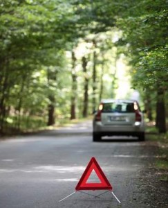 Un triangle de signalisation rouge est placé sur une route forestière près de Chambly, avec une voiture argentée garée au bord de la route sous de grands arbres verts, un rappel de l'importance de l'assurance automobile.