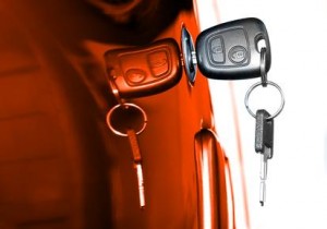 Une clé de voiture insérée dans la serrure d'une portière, avec un porte-clés et un anneau attachés. La portière reflète la clé et le porte-clés, créant un effet miroir. Des tons orange et blanc teintent l'image, évoquant un sentiment d'assurance et de sécurité.