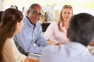 Quatre personnes sont assises à une table dans un bureau et discutent de leur copropriété. Deux d'entre elles font face à la caméra, tandis que les deux autres se détournent, suggérant une assemblée des copropriétaires collaborative ou une discussion d'équipe.